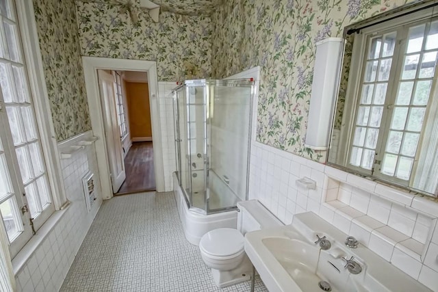 bathroom with tile walls, combined bath / shower with glass door, tile patterned floors, and toilet