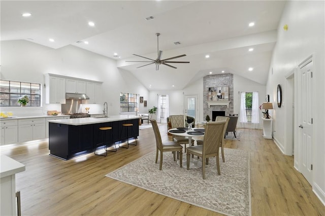 dining area featuring high vaulted ceiling, sink, a fireplace, and light hardwood / wood-style floors