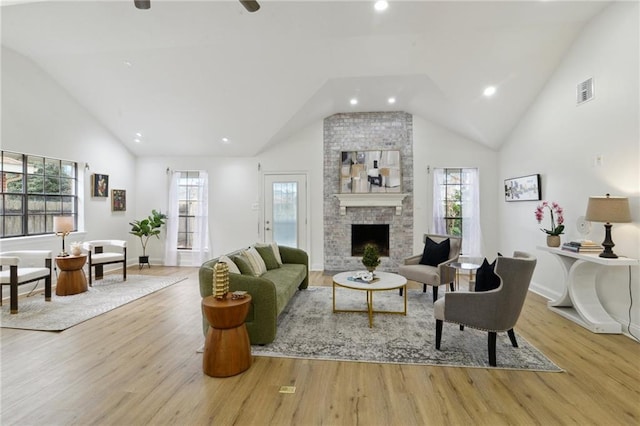 living room featuring high vaulted ceiling, a large fireplace, and light wood-type flooring