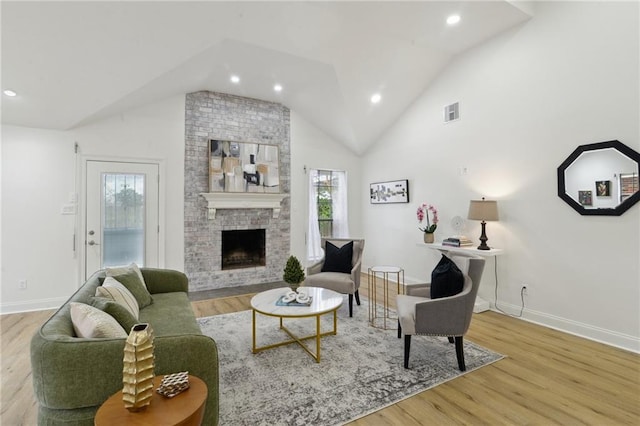 living room with a brick fireplace, lofted ceiling, and light hardwood / wood-style flooring