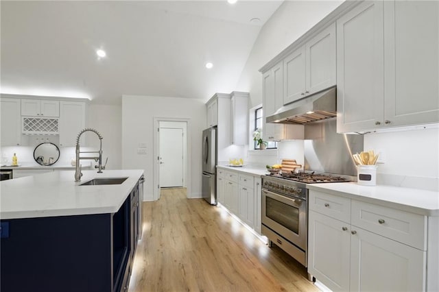 kitchen featuring lofted ceiling, sink, appliances with stainless steel finishes, a center island with sink, and light wood-type flooring