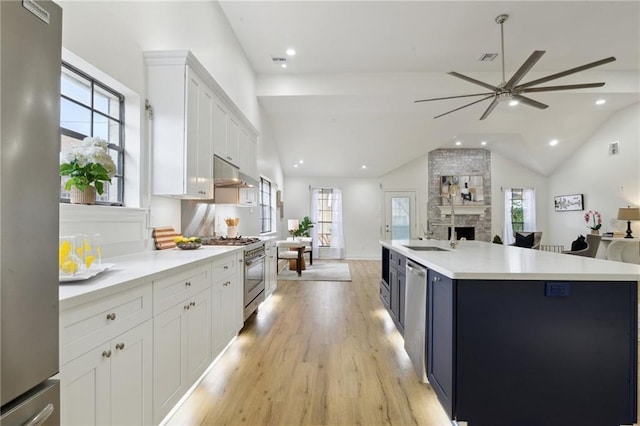 kitchen with white cabinetry, vaulted ceiling, light wood-type flooring, a large fireplace, and appliances with stainless steel finishes