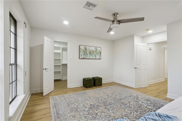 bedroom with ceiling fan, a walk in closet, and light wood-type flooring