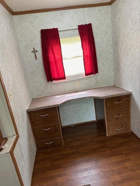 unfurnished office featuring ornamental molding, dark wood-type flooring, and built in desk