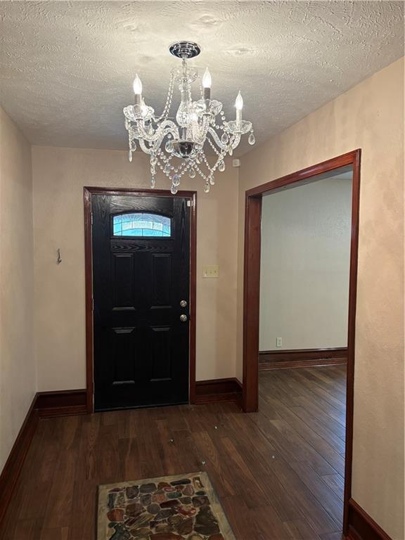 foyer entrance featuring an inviting chandelier, dark wood-type flooring, and a textured ceiling