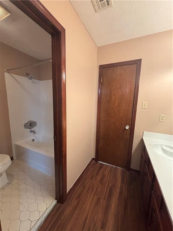 full bathroom with bathtub / shower combination, toilet, a textured ceiling, vanity, and hardwood / wood-style floors