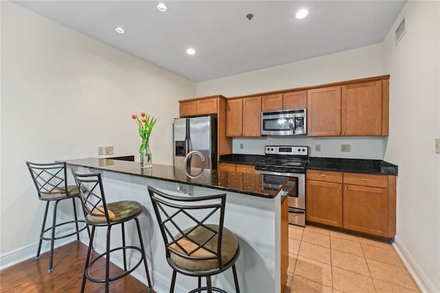 kitchen with dark stone countertops, a kitchen bar, light tile patterned floors, and appliances with stainless steel finishes