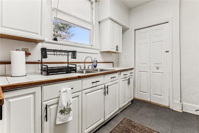 kitchen featuring dark tile patterned floors, sink, tile countertops, and white cabinets