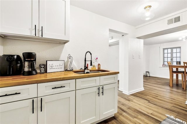 bar featuring white cabinets, sink, light hardwood / wood-style flooring, and butcher block countertops