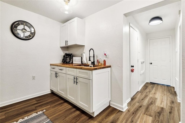 bar featuring butcher block countertops, dark hardwood / wood-style floors, sink, and white cabinets