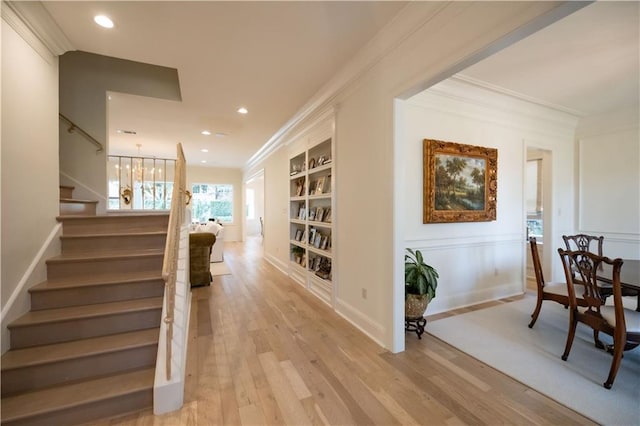 hall featuring built in shelves, ornamental molding, an inviting chandelier, and light hardwood / wood-style floors