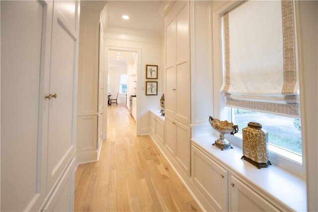 hall with ornamental molding, a healthy amount of sunlight, and light hardwood / wood-style floors