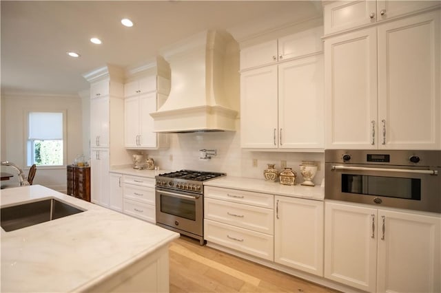 kitchen featuring sink, ornamental molding, appliances with stainless steel finishes, custom range hood, and white cabinets