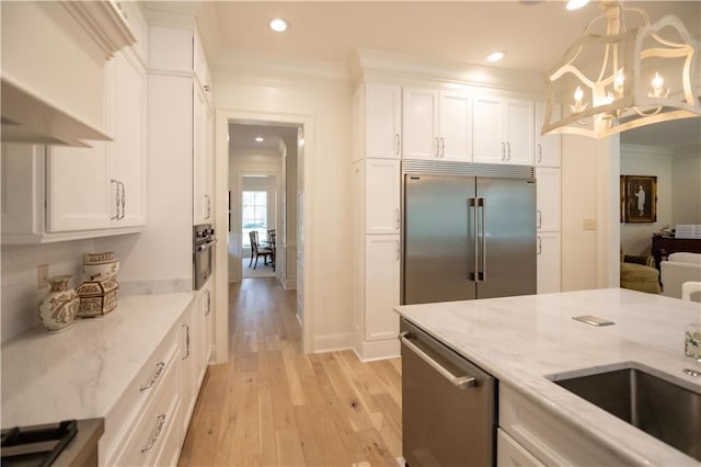 kitchen with white cabinetry, light stone counters, crown molding, decorative light fixtures, and stainless steel appliances