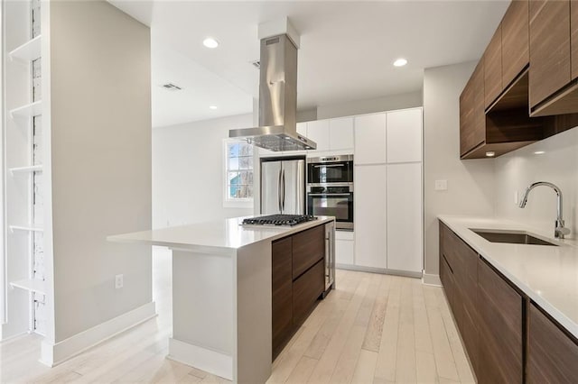 kitchen with sink, appliances with stainless steel finishes, white cabinets, island exhaust hood, and light wood-type flooring