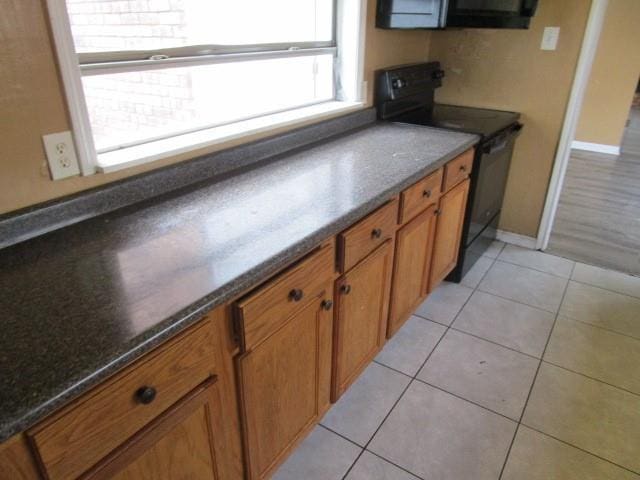 kitchen with black / electric stove, dark stone countertops, and light tile patterned floors