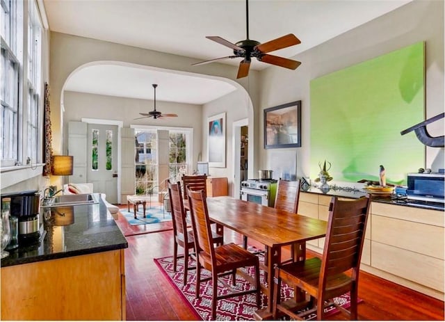 dining room featuring arched walkways, dark wood finished floors, and ceiling fan