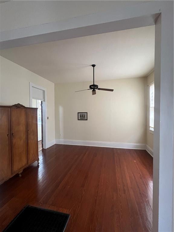 unfurnished living room with a ceiling fan, baseboards, and dark wood-type flooring