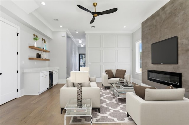 living room featuring wine cooler, ornamental molding, a fireplace, and light hardwood / wood-style flooring