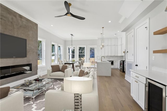 living room featuring sink, a fireplace, light hardwood / wood-style floors, ornamental molding, and beverage cooler