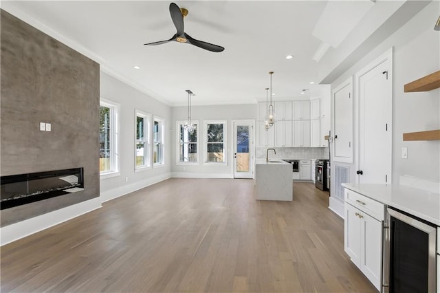 unfurnished living room featuring wine cooler, sink, ornamental molding, hardwood / wood-style flooring, and a fireplace