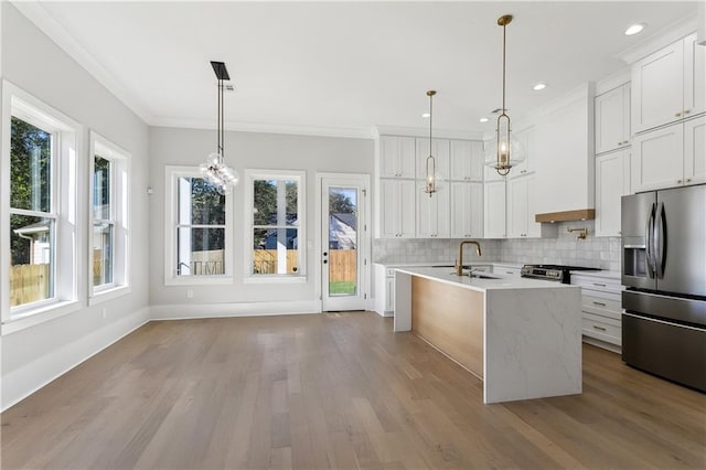 kitchen with appliances with stainless steel finishes, white cabinets, a center island with sink, decorative light fixtures, and custom exhaust hood