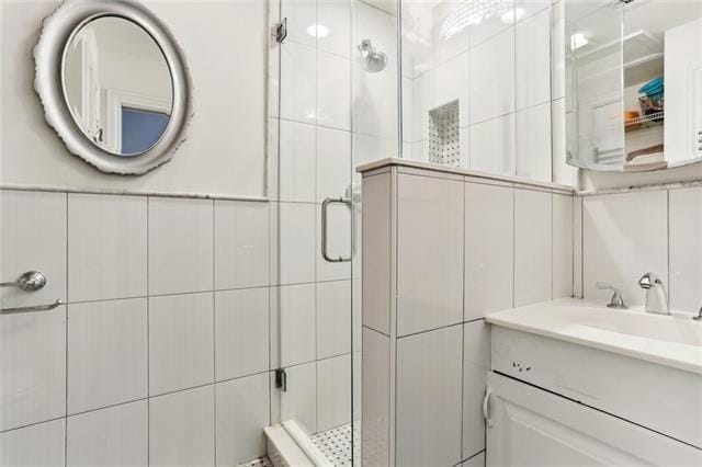 bathroom with vanity, a shower with door, and tile walls