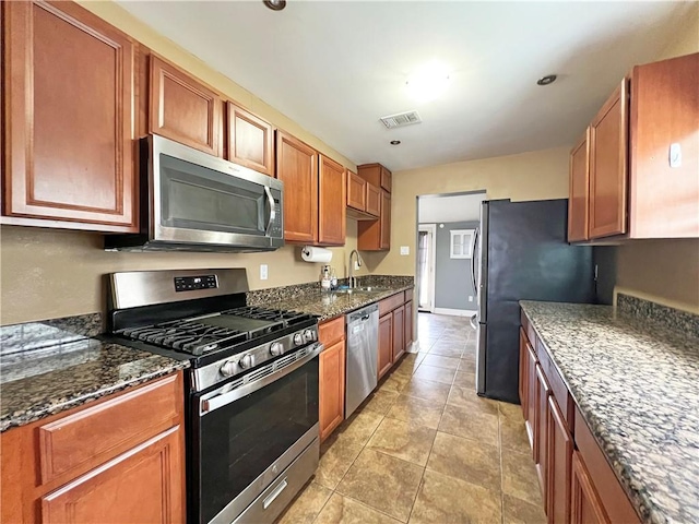 kitchen with appliances with stainless steel finishes, sink, dark stone countertops, and light tile patterned floors