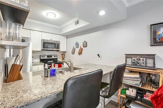 kitchen featuring white cabinetry, crown molding, appliances with stainless steel finishes, a kitchen breakfast bar, and light stone countertops