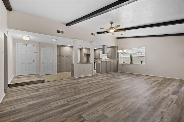 unfurnished living room featuring lofted ceiling with beams, hardwood / wood-style flooring, ceiling fan with notable chandelier, and a textured ceiling