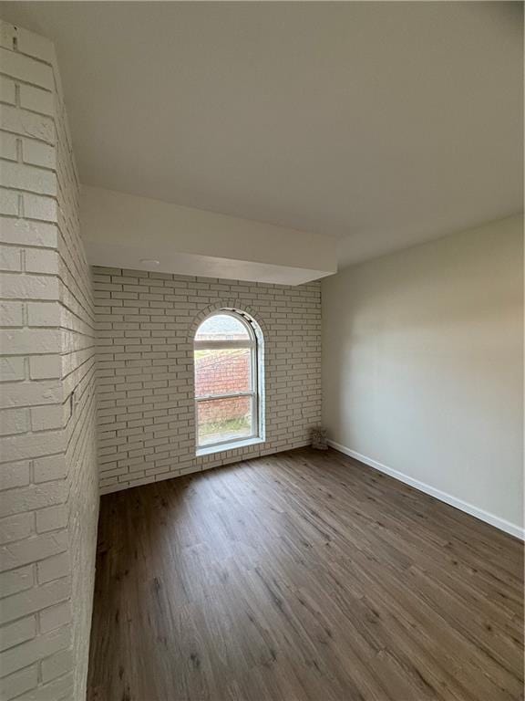 unfurnished room with dark hardwood / wood-style floors and brick wall