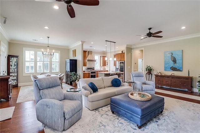 living room with ornamental molding, ceiling fan with notable chandelier, and light wood-type flooring