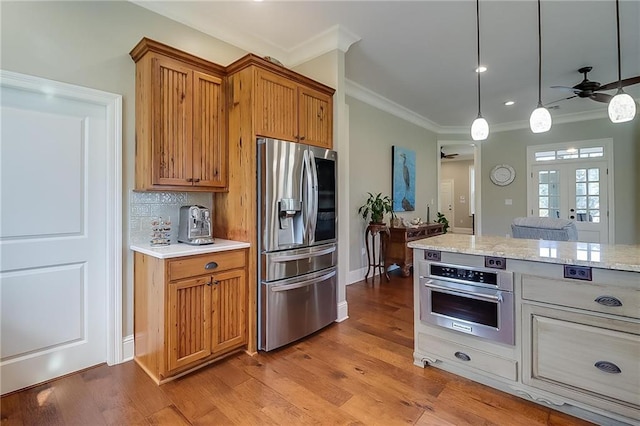 kitchen featuring crown molding, appliances with stainless steel finishes, hanging light fixtures, and light wood-type flooring