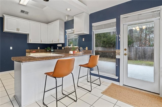 kitchen with light tile patterned flooring, kitchen peninsula, white cabinets, and a breakfast bar