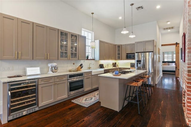 kitchen with appliances with stainless steel finishes, beverage cooler, hanging light fixtures, a center island, and a barn door