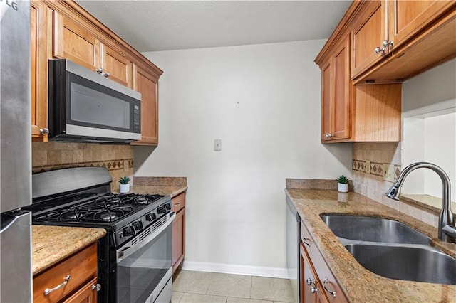 kitchen with sink, light tile patterned floors, stainless steel appliances, light stone countertops, and decorative backsplash