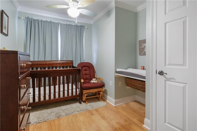 bedroom with ornamental molding, a nursery area, wood-type flooring, and ceiling fan