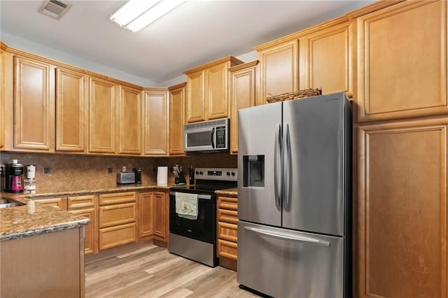 kitchen featuring appliances with stainless steel finishes, light brown cabinetry, decorative backsplash, light stone countertops, and light wood-type flooring