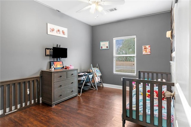 bedroom with dark wood-type flooring, ceiling fan, and a nursery area