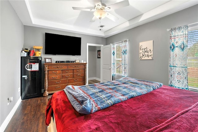 bedroom featuring a tray ceiling, dark hardwood / wood-style floors, and ceiling fan