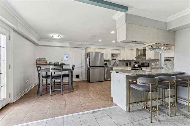 kitchen with a kitchen bar, light tile patterned floors, cream cabinetry, stainless steel appliances, and wall chimney exhaust hood