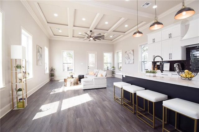 kitchen featuring a kitchen bar, coffered ceiling, crown molding, pendant lighting, and white cabinets