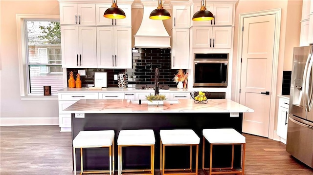 kitchen with pendant lighting, appliances with stainless steel finishes, white cabinetry, light stone counters, and a kitchen island