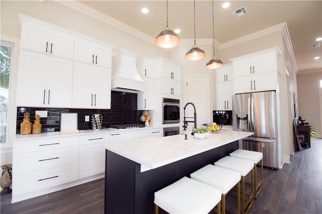 kitchen with stainless steel appliances, premium range hood, a kitchen island with sink, and white cabinets