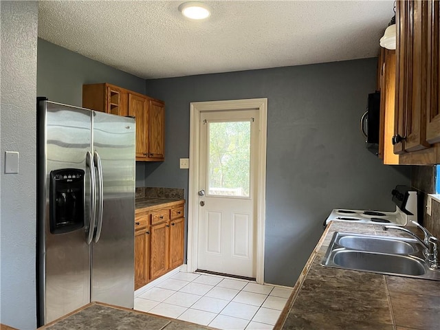 kitchen featuring stainless steel refrigerator with ice dispenser, light tile patterned flooring, sink, and a textured ceiling