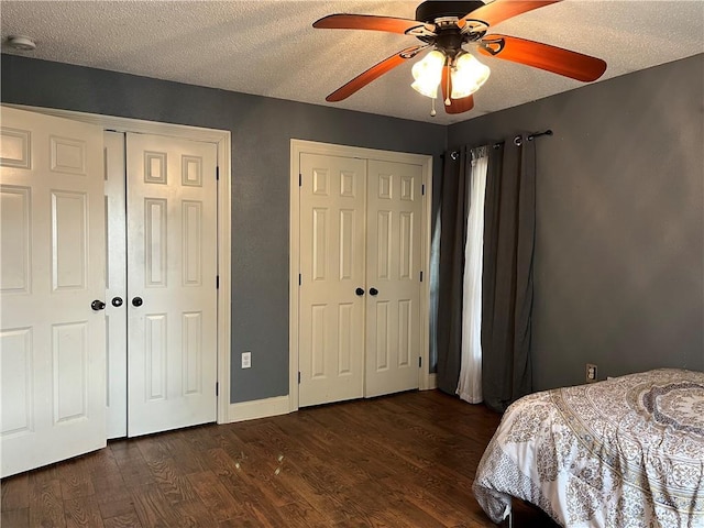 bedroom with multiple closets, ceiling fan, dark wood-type flooring, and a textured ceiling