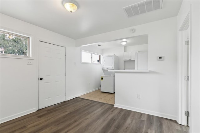 interior space with dark hardwood / wood-style floors, stacked washing maching and dryer, kitchen peninsula, and white cabinets