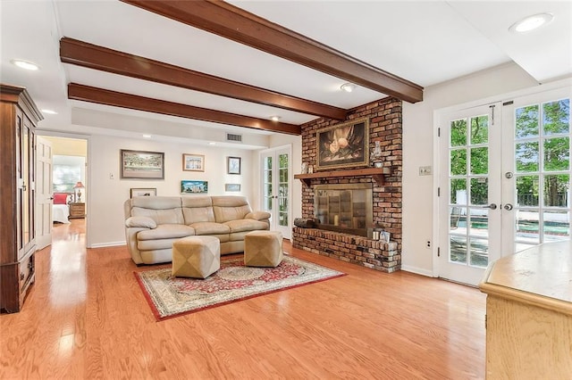 living room featuring french doors, a fireplace, light hardwood / wood-style flooring, and beamed ceiling