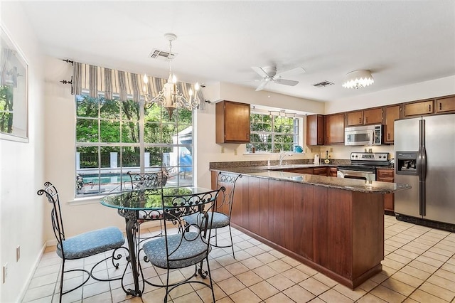 kitchen with light tile patterned floors, appliances with stainless steel finishes, hanging light fixtures, ceiling fan with notable chandelier, and kitchen peninsula