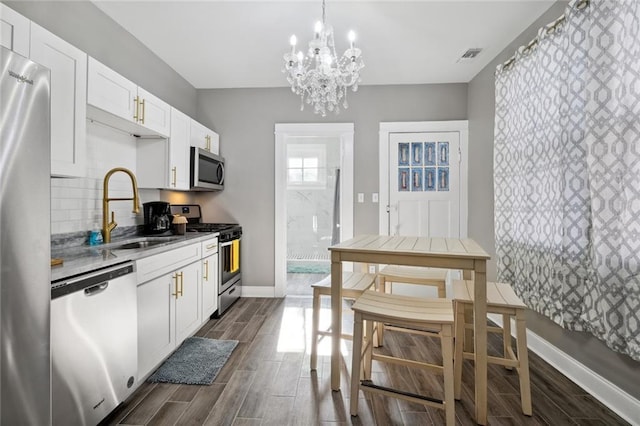 kitchen featuring sink, white cabinets, pendant lighting, stainless steel appliances, and backsplash